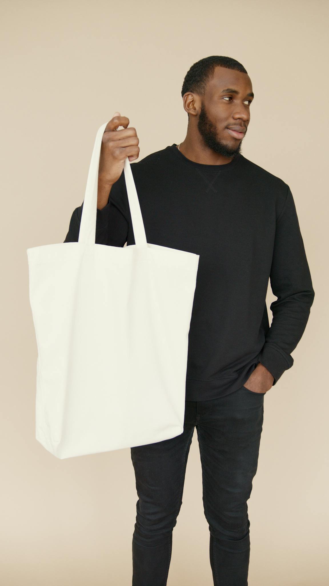 Fashionable man holding a minimalist white tote bag against a neutral background.