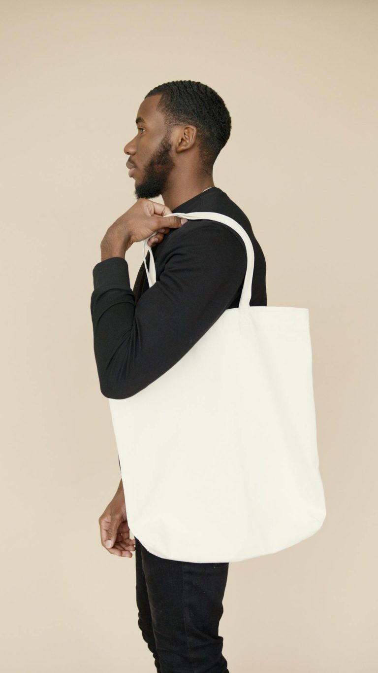 Profile of a young man holding a white tote bag, showcasing eco-fashion.